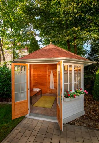 a wooden gazebo with a bench and flowers at Hotel Schweizer Hof Thermal und Vital Resort in Bad Füssing