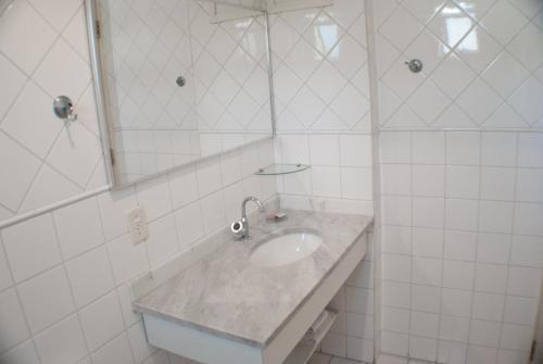 a white tiled bathroom with a sink and a mirror at Residencial Bella Vista Suites in Sao Paulo