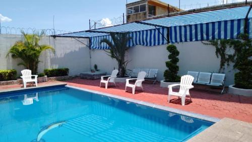 a swimming pool with white chairs and a blue and white umbrella at Family villa in Tequesquitengo