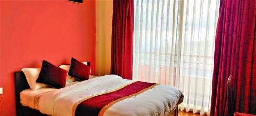 a bedroom with a bed with red walls and a window at Hotel Nagarkot Inn in Nagarkot