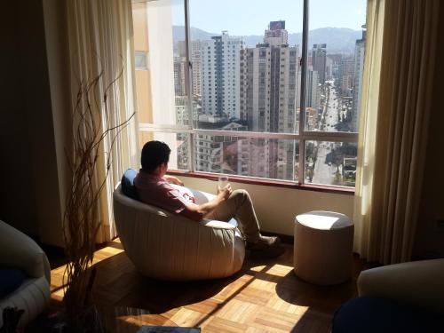 un hombre sentado en una silla frente a una ventana en APARTAMENTO PRIVADO Piso 20a, CENTRICO, CERCA EMBAJADA USA, TELEFERICO, MALLS, VISTAS 360 y ZONA SEGURA, en La Paz