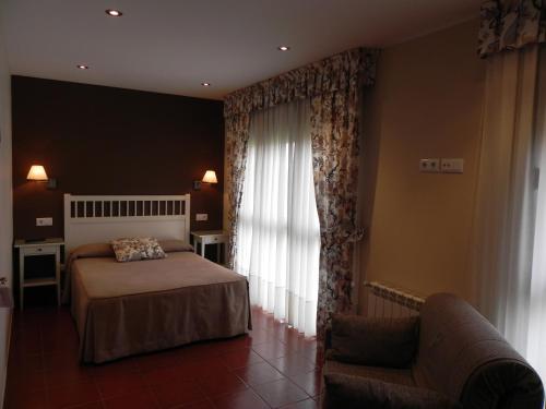 a bedroom with a bed and a chair and a window at Hospederia Los Pinos in Llanes