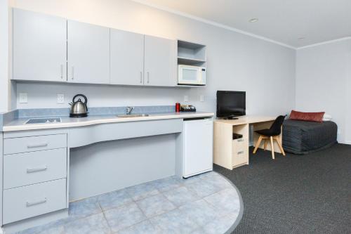 a kitchen with white cabinets and a sink and a couch at Aubyn Court Spa Motel in Palmerston North