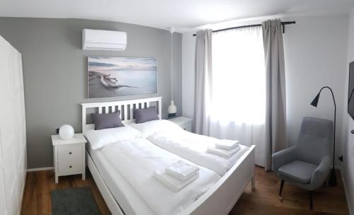 ein weißes Schlafzimmer mit einem großen Bett und einem Stuhl in der Unterkunft Storchennest-Appartements in Rust