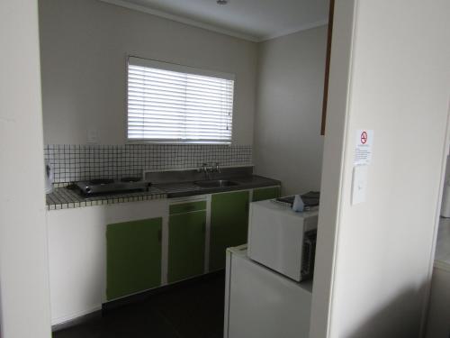 a kitchen with green cabinets and a sink and a window at Anchorage Motel in Whitianga