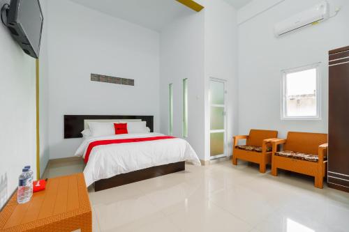 a white bedroom with a bed and two chairs at RedDoorz Syariah near Simpang Sekip Palembang in Palembang