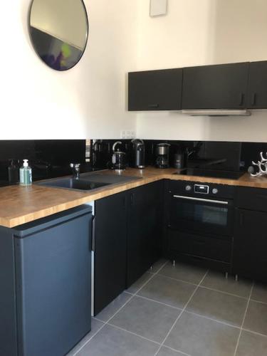 eine Küche mit schwarzen Schränken, einem Waschbecken und einem Spiegel in der Unterkunft Appartement avec terrasse panoramique au coeur de Nîmes in Nîmes