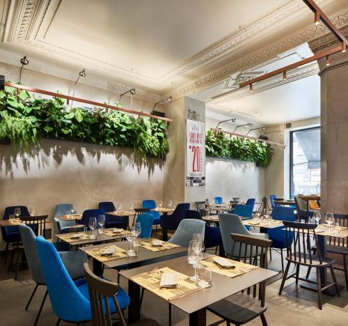 un restaurante con mesas, sillas y plantas en la pared en The Modernist Hotel en Trieste