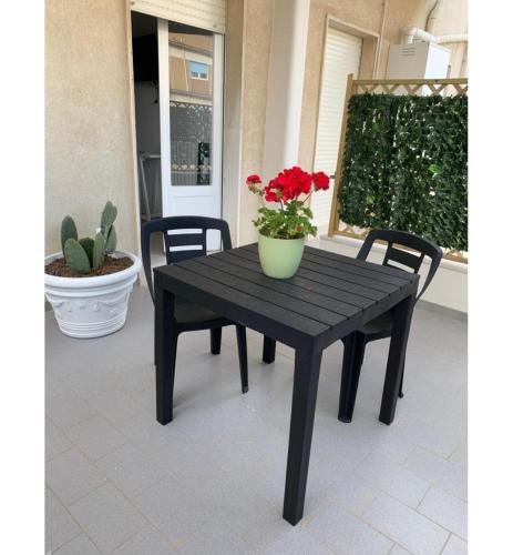a black table with two chairs and a vase with red flowers at Mini appartamento Aria in OstuniCrispiHouse in Ostuni