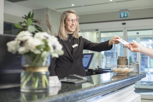 a woman standing at a counter giving a receipt at Hotel Villa Rosa Riviera in Rimini