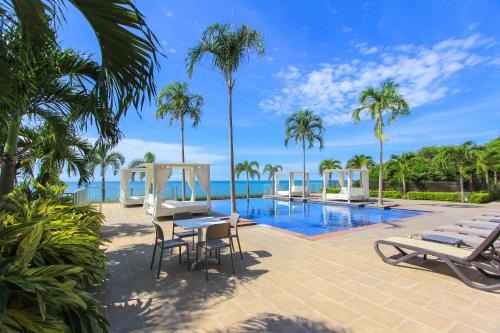 a resort pool with chairs and palm trees and the ocean at 2201 Playa EL Palmar in Las Palmeras