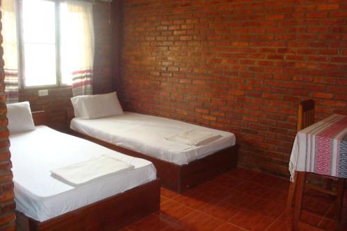 two beds in a room with a brick wall at Zuela Guesthouse in Louang Namtha