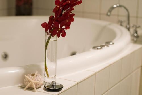 a vase with red flowers on a counter next to a bath tub at The Moorings at Metung in Metung