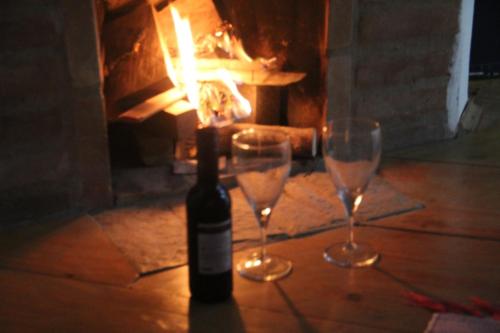 a bottle of wine and two glasses in front of a fireplace at Chalés Luz da Montanha in Núcleo Mauá