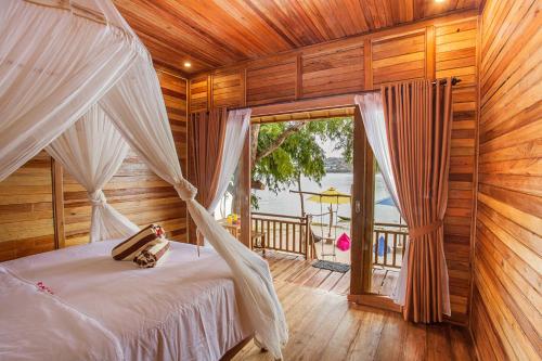 ein Schlafzimmer mit einem Himmelbett und einem Balkon in der Unterkunft Wooden Beach Sunset Cottages in Nusa Lembongan