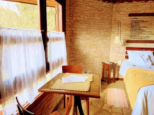 a room with two beds and a table and a window at Pousada Cantinho das Estrelas in Monte Verde