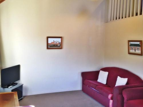 a living room with a red couch and a tv at Woodlands Motels And Apartments in Dunedin