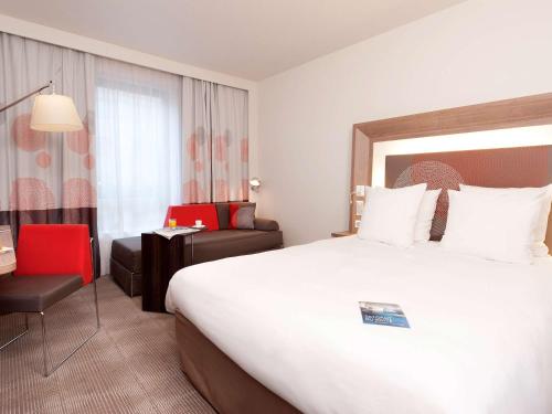 a hotel room with a large bed and a red chair at Novotel Paris Rueil Malmaison in Rueil-Malmaison
