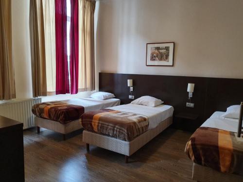 two beds in a hotel room with red curtains at Hotel Queen Mary in Brussels