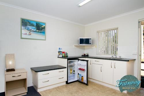 a kitchen with white cabinets and a refrigerator at Fairway Motor Inn in Merimbula