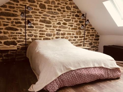 Bett in einem Zimmer mit einer Steinmauer in der Unterkunft Maison en pierre entièrement rénovée. in Trébry