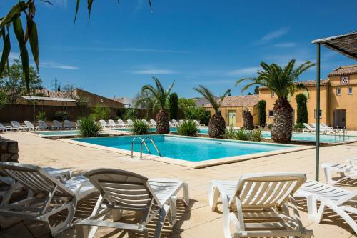 une piscine avec des chaises longues et un complexe hôtelier dans l'établissement SOWELL RESIDENCES Les Mazets, à Arles