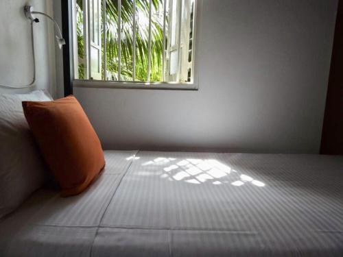 1 cama con almohada naranja en una habitación con ventana en HappyShack Hostel, en Mirissa