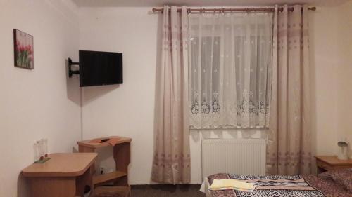 a bedroom with a window with curtains and a television at PENZION EUROPA Diakovce in Diakovce