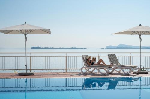 a woman laying in chairs next to a swimming pool at Hotel Villa Florida Suites & Suite Apartments in Gardone Riviera
