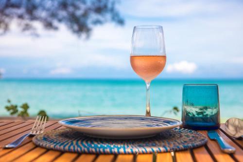 a glass of wine sitting on a table near the ocean at Twinpalms MontAzure Phuket in Kamala Beach