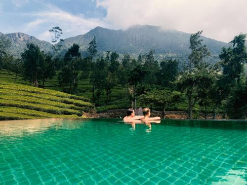 two people sitting in a swimming pool with mountains in the background at Tea and Experience Factory - Thema Collection in Mandaran Newara