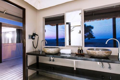 two sinks on a counter in a bathroom with windows at Dead Valley Lodge in Sesriem