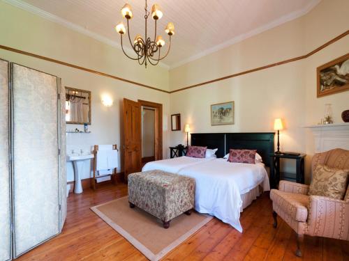 a bedroom with a bed and a chair and a chandelier at Leeuwenbosch Country House - Amakhala Game Reserve in Amakhala Game Reserve