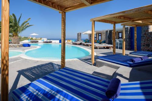 a swimming pool with blue lounge chairs and a resort at Anemomilos in Oia