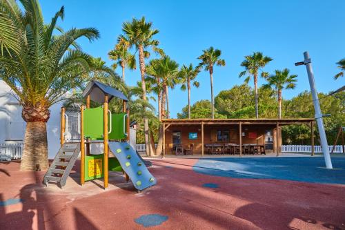 a playground in front of a building with palm trees at Hipotels Mediterraneo Club in Sa Coma