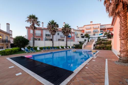 a swimming pool in front of a building with palm trees at Acolhedora Vivenda Geminada Praia D'el Rey in Casal da Lagoa Seca
