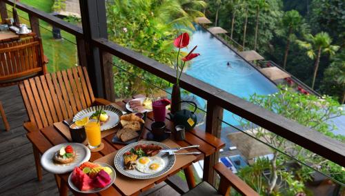 a table with breakfast food on a balcony with a pool at Chapung Sebali Resort in Ubud
