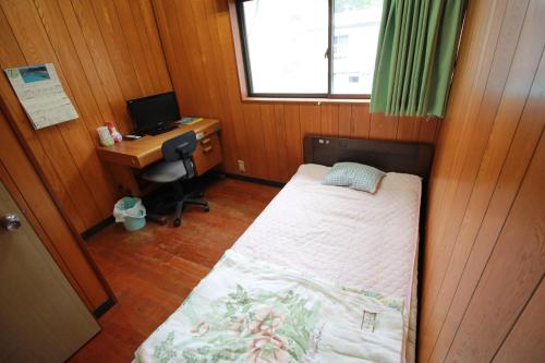 a small bedroom with a bed and a desk with a computer at Guest House Aman in Amami