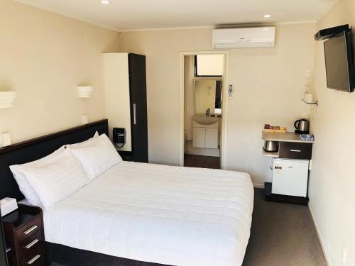 a bedroom with a white bed and a bathroom at Tudor Court Motor Lodge in Auckland