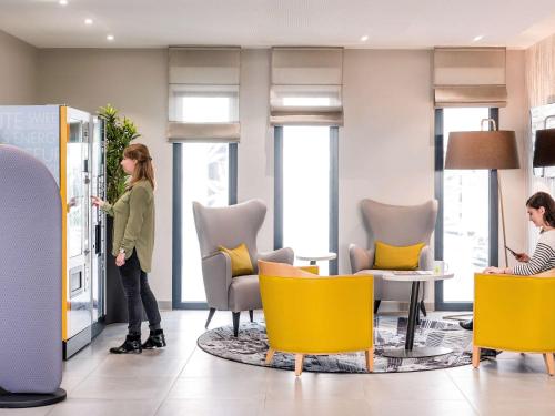 a woman standing in a lobby with yellow chairs at Aparthotel Adagio access Colombes La Défense in Colombes