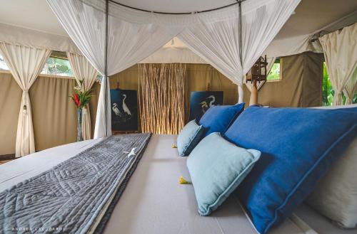 a bedroom with a canopy bed with blue pillows at Sandat Glamping Tents in Ubud