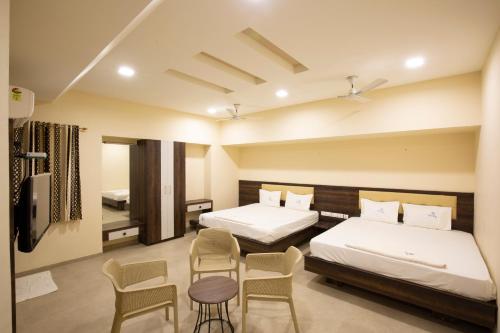 two beds in a room with two chairs and a table at Ponnis Hotel in Palani