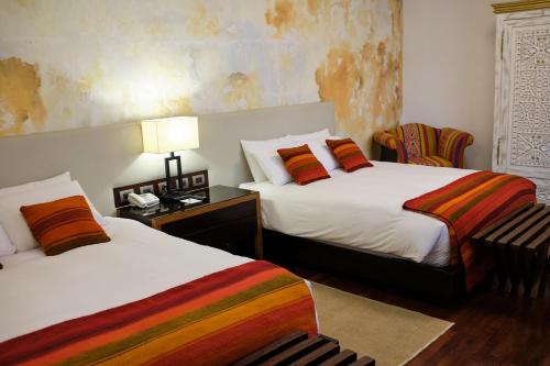 a bedroom with two beds and a table with a lamp at Tocuyeros Boutique Hotel in Cusco