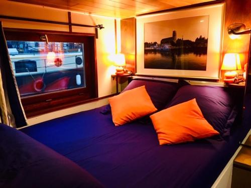 een paars bed met 2 oranje kussens naast een raam bij La bigoudène in Wambrechies