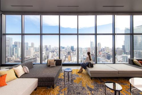 a woman sitting on a couch in a room with large windows at THE BLOSSOM HIBIYA in Tokyo