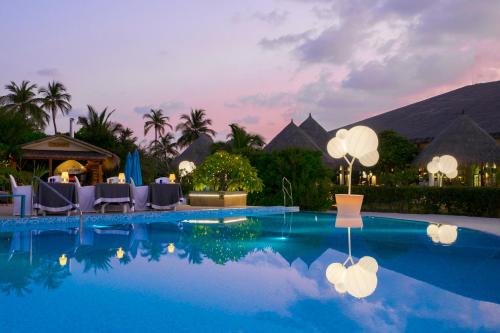 a pool at a resort with tables and chairs at Cocoon Maldives - All Inclusive in Lhaviyani Atoll