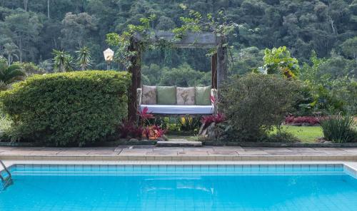 a pool with a couch sitting next to a garden at Pousada Quinta dos Pássaros Itaipava in Itaipava
