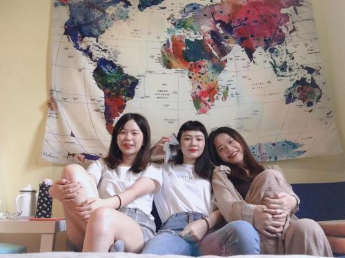 three girls sitting on a bed in front of a world map at mydeer backpacker in Tainan