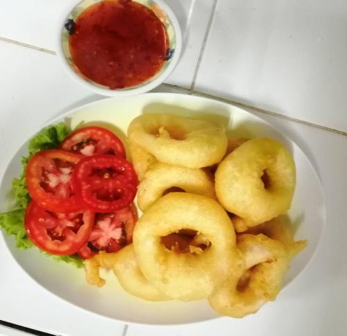 a white plate of food with onion rings and tomatoes at Tony Home and Restaurant in Karon Beach