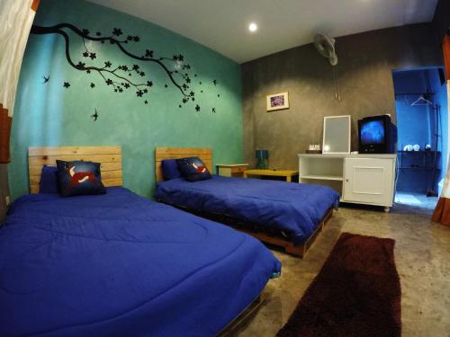 een slaapkamer met 2 bedden met blauwe lakens en een muurschildering van bomen bij Payi Resort in Pai